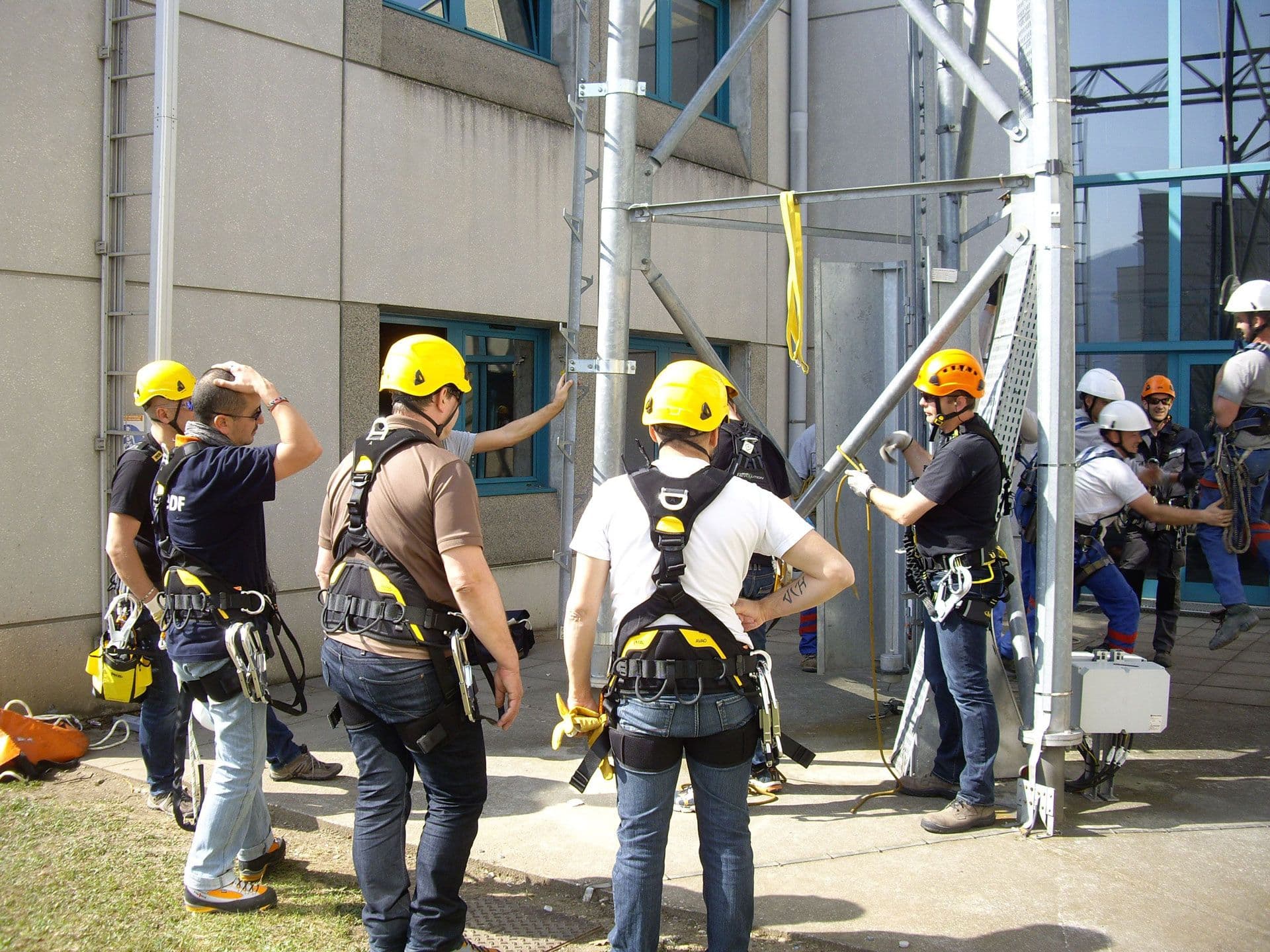Workers in hard hats and safety harnesses gathered around scaffolding for training.