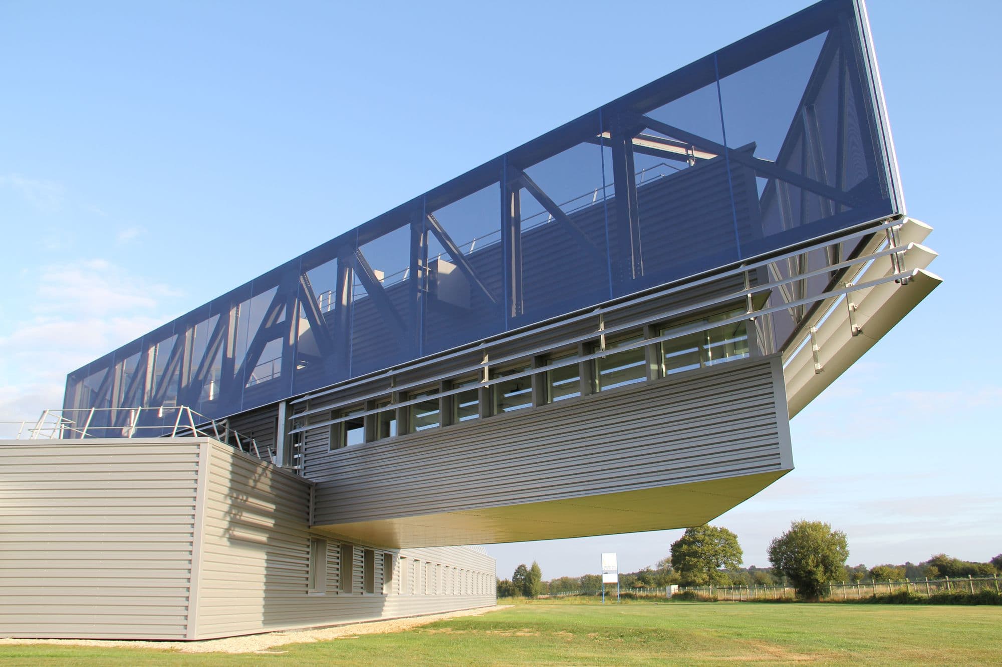 Modern angular building with a dark blue perforated metal top section against a blue sky.